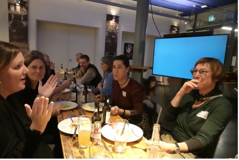 A picture of a long table with lots of people talking and eating